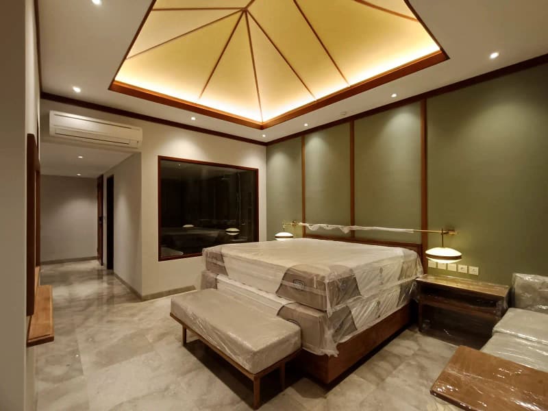Interior kamar utama villa dengan pencahayaan cove tersembunyi pada plafon dan dinding panel kayu